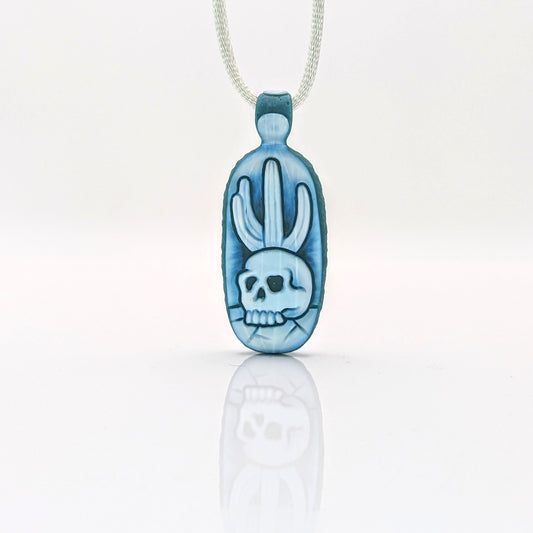 Kellie Thurston Skull & Cactus (Aqua Azul under Lotus White), 2024 Borosilicate Glass Pendant 60 mm x 24 mm Hand carved borosilicate glass pendant by Kellie Thurston. Prep by Dan Longden.