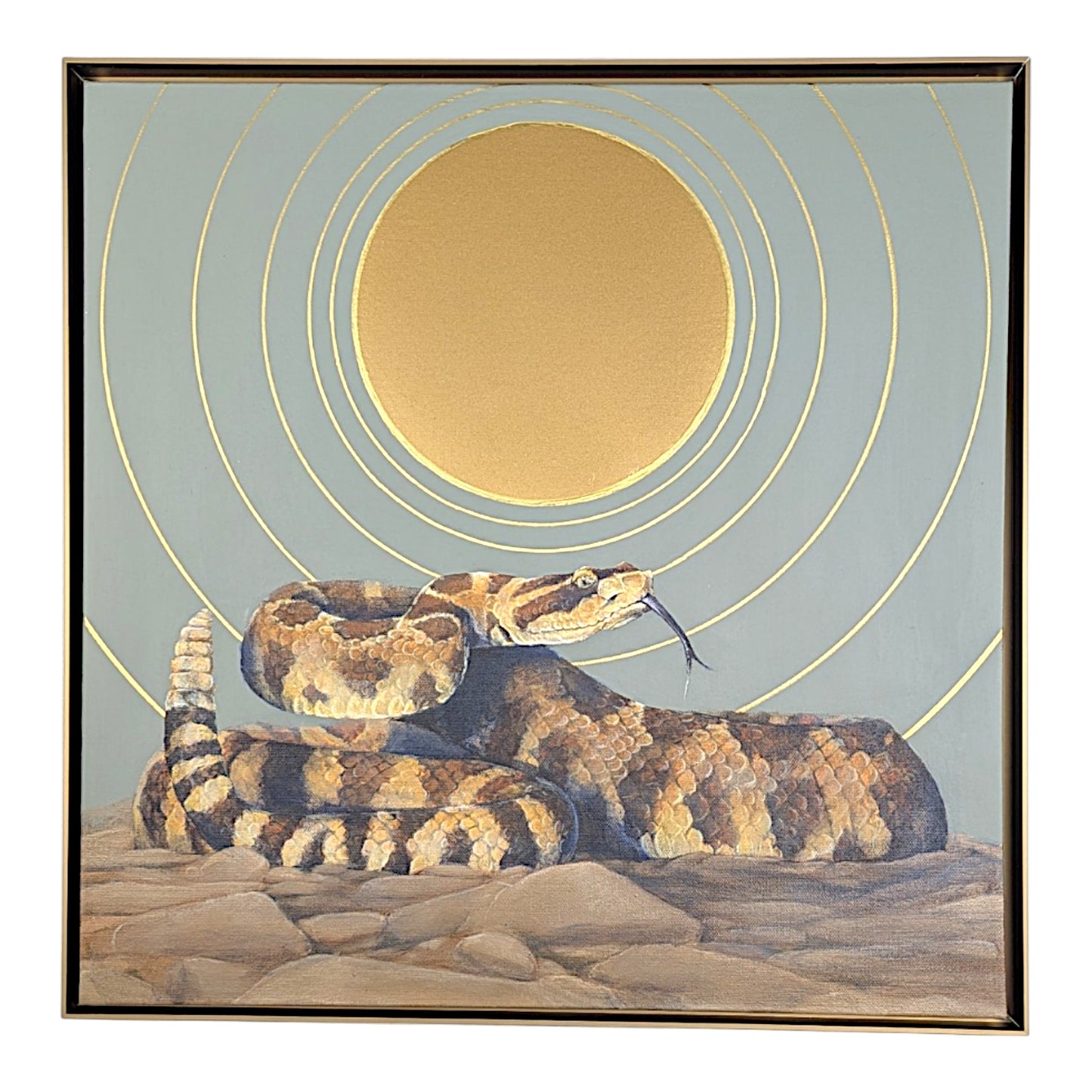 A framed square art print depicting a coiled rattlesnake on rocky ground beneath concentric gold rings around a large gold sun on a muted blue-gray background.