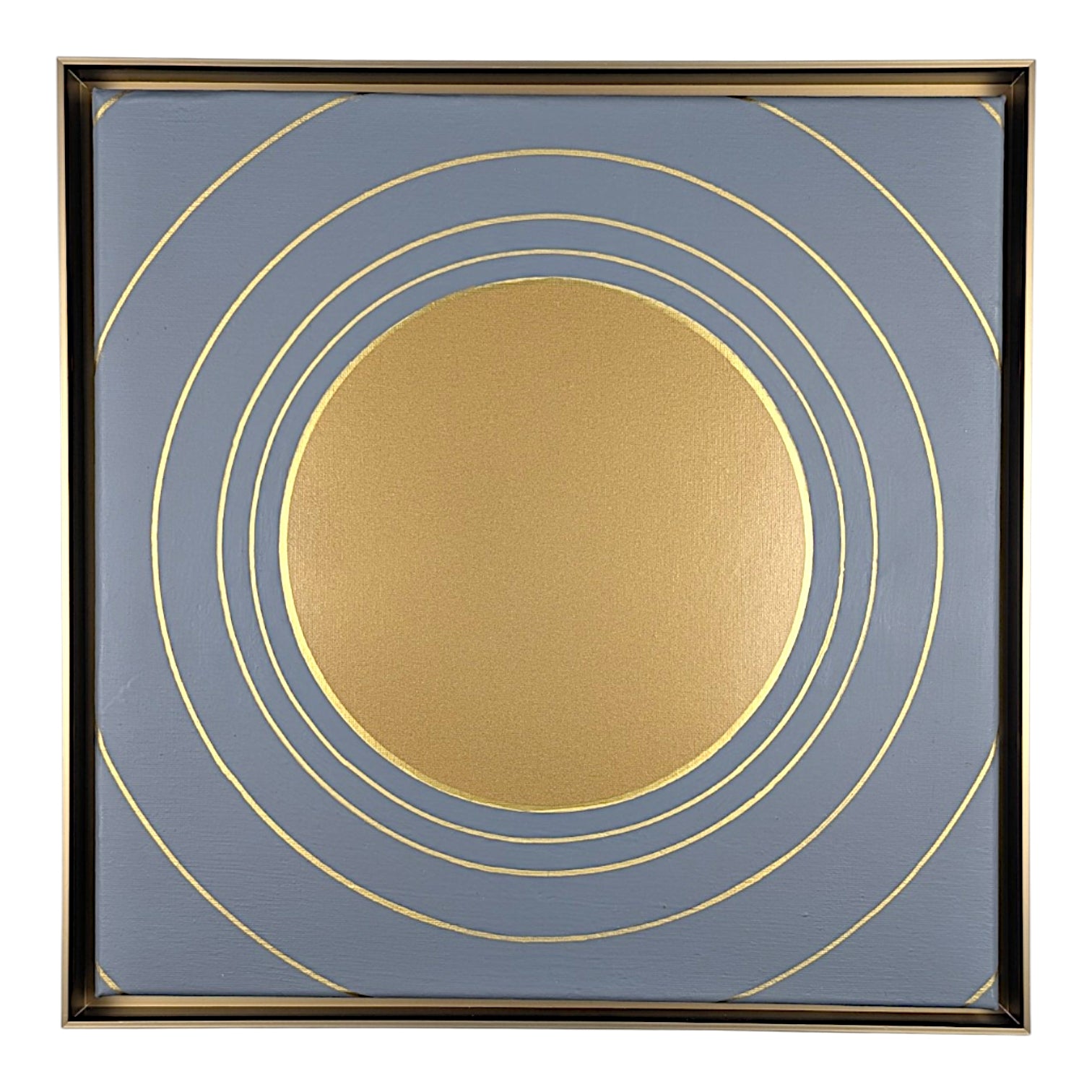 Square framed wall art featuring a large metallic gold circle at the center with multiple thin gold concentric rings on a muted blue-gray background, surrounded by a dark frame.