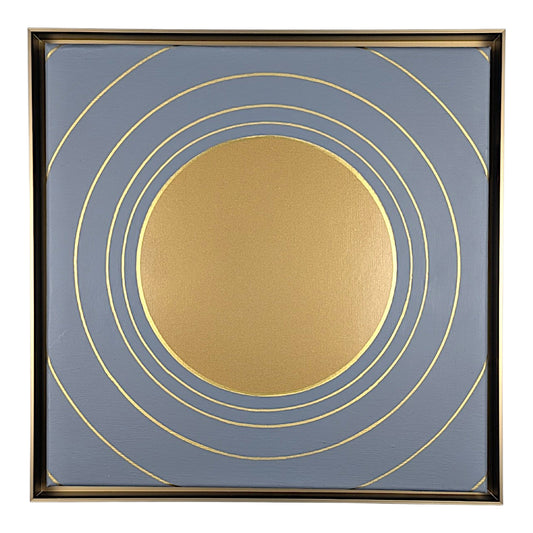Square framed wall art featuring a large metallic gold circle at the center with multiple thin gold concentric rings on a muted blue-gray background, surrounded by a dark frame.